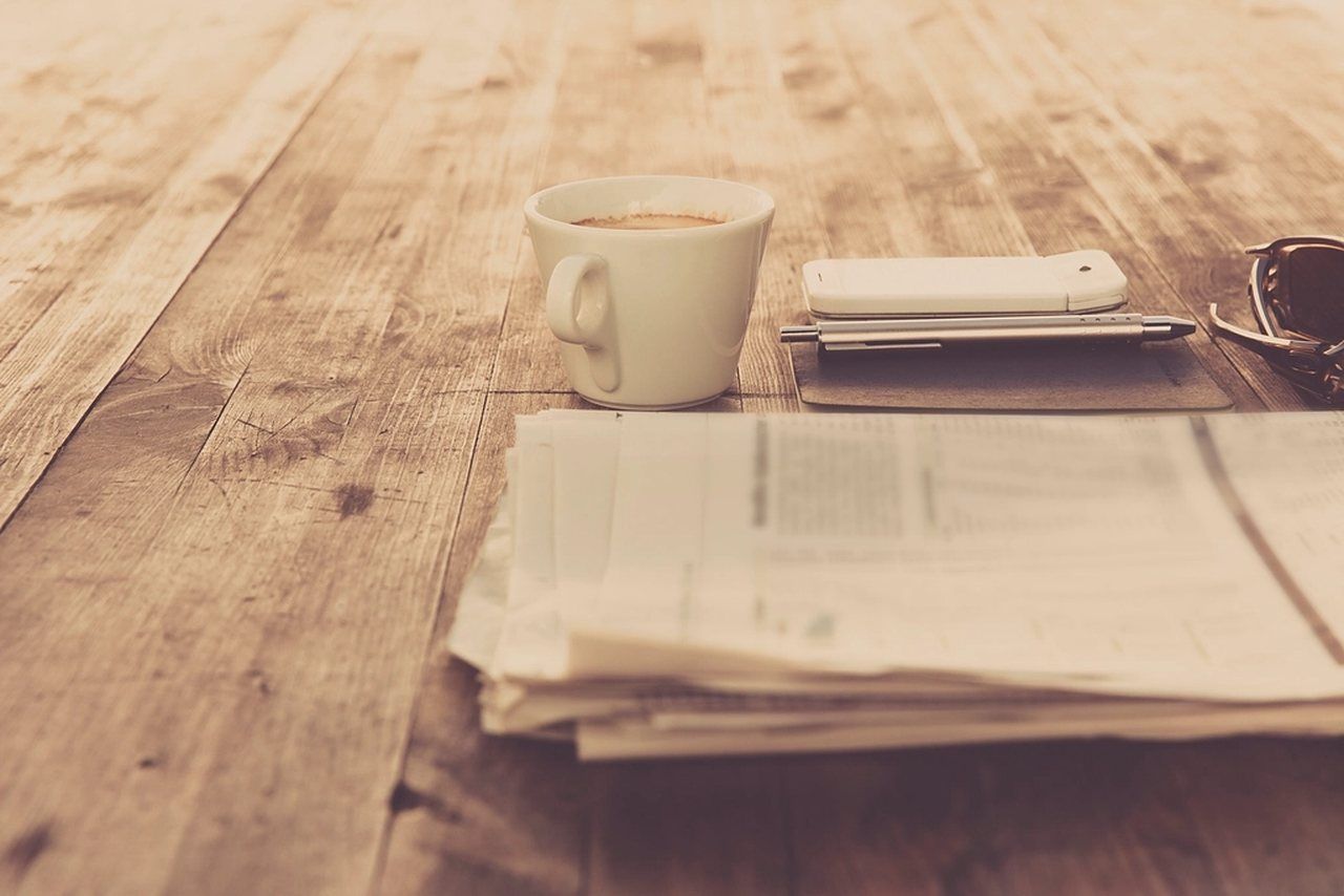 Zusammengefaltete Zeitung, Kaffeetasse und Smartphone auf einem Holztisch